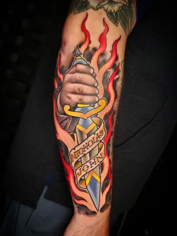 Dagger through a hand with flames and name banner by Chris Carp at Heart & Sword Tattoo