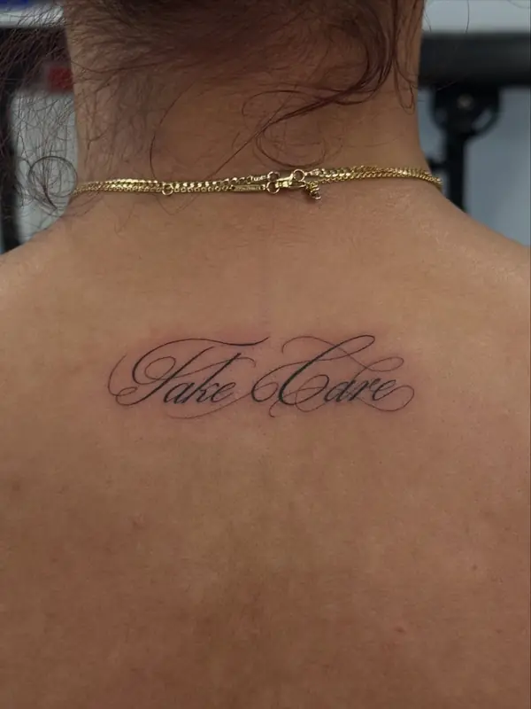 Fine line 'Take Care' script on upper back by Dina at Heart & Sword Tattoo